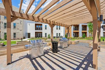 A wooden pergola over a patio with a grill and trash can.